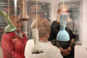 Kolorowe telefony w szklanej gablocie. W tle zwiedzający wystawę.