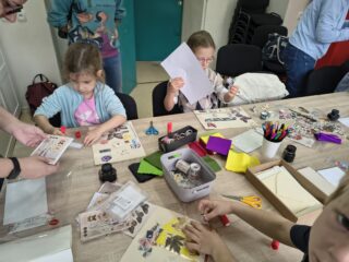 dwójka dzieci przy stole, zajęta ozdabianiem kartek i listów materiałami plastycznymi.