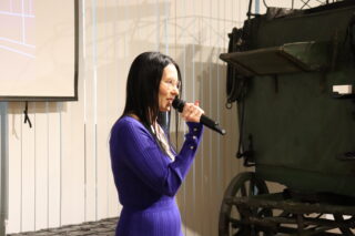 Dyrektor Muzeum przemawia, trzymając mikrofon. W tle furgon pocztowy.