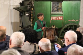 Publiczność ogląda prezentację przy historycznej instalacji telefonicznej w kolorze zielonym.