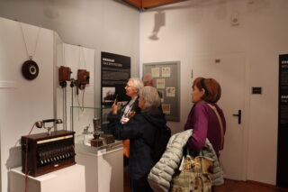 Zwiedzający oglądają ścienny zestaw historycznych aparatów telefonicznych