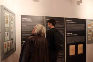Zwiedzający oglądają plansze i gabloty z dokumentami i zdjęciami archiwalnymi.