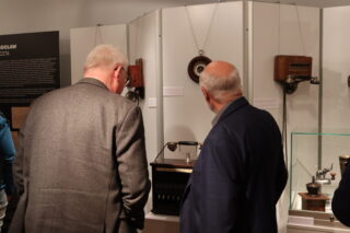 Dwóch zwiedzających rozmawia przy gablocie z urządzeniami telekomunikacyjnymi.