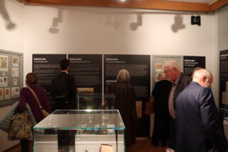 Zwiedzający oglądają ekspozycję z mapami, dokumentami i urządzeniami łączności.