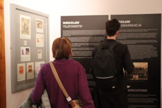 Para zwiedzających czyta planszę informacyjną na wystawie.