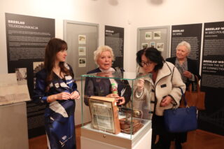 Prowadząca i dwie osoby prezentują eksponat w centralnej gablocie.