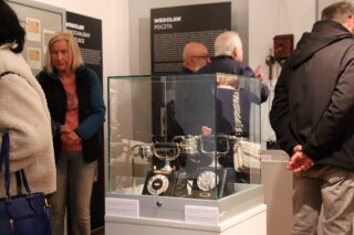 Zwiedzający oglądają szklaną gablotę z historycznymi aparatami telefonicznymi.