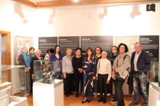 Grupowe zdjęcie uczestników wydarzenia na tle plansz wystawy telekomunikacyjnej.