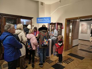 Grupa dzieci i dorosłych czeka przy stanowisku informacyjnym