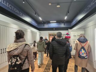 Grupa zwiedzających przechodzi przez salę z kolekcją polskich znaczków pocztowych.