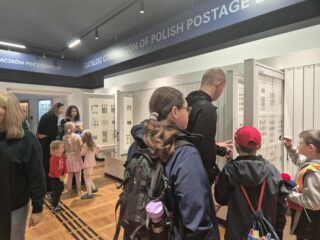 Dzieci i dorośli oglądają ekspozycję polskich znaczków pocztowych.