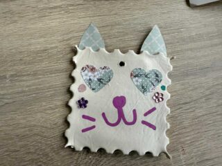 Ozdoba choinkowa w kształcie znaczka pocztowego, z dodanymi uszami, przypominająca kota.